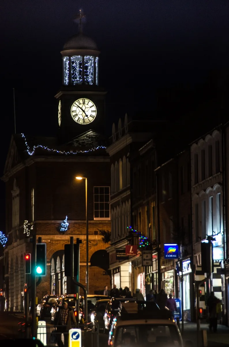Bridport Town Hall clock tower lit with blue and white Christmas lights at night, with shops along East Street