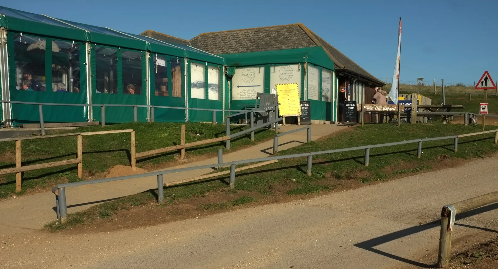The Hive Beach Café at Burton Bradstock, a long green-and-glass building above the beach path, with a queue board by the door