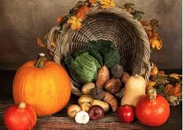 A wicker basket of cabbage, carrots, potatoes and onions on a wooden table with pumpkins, squash and autumn leaves