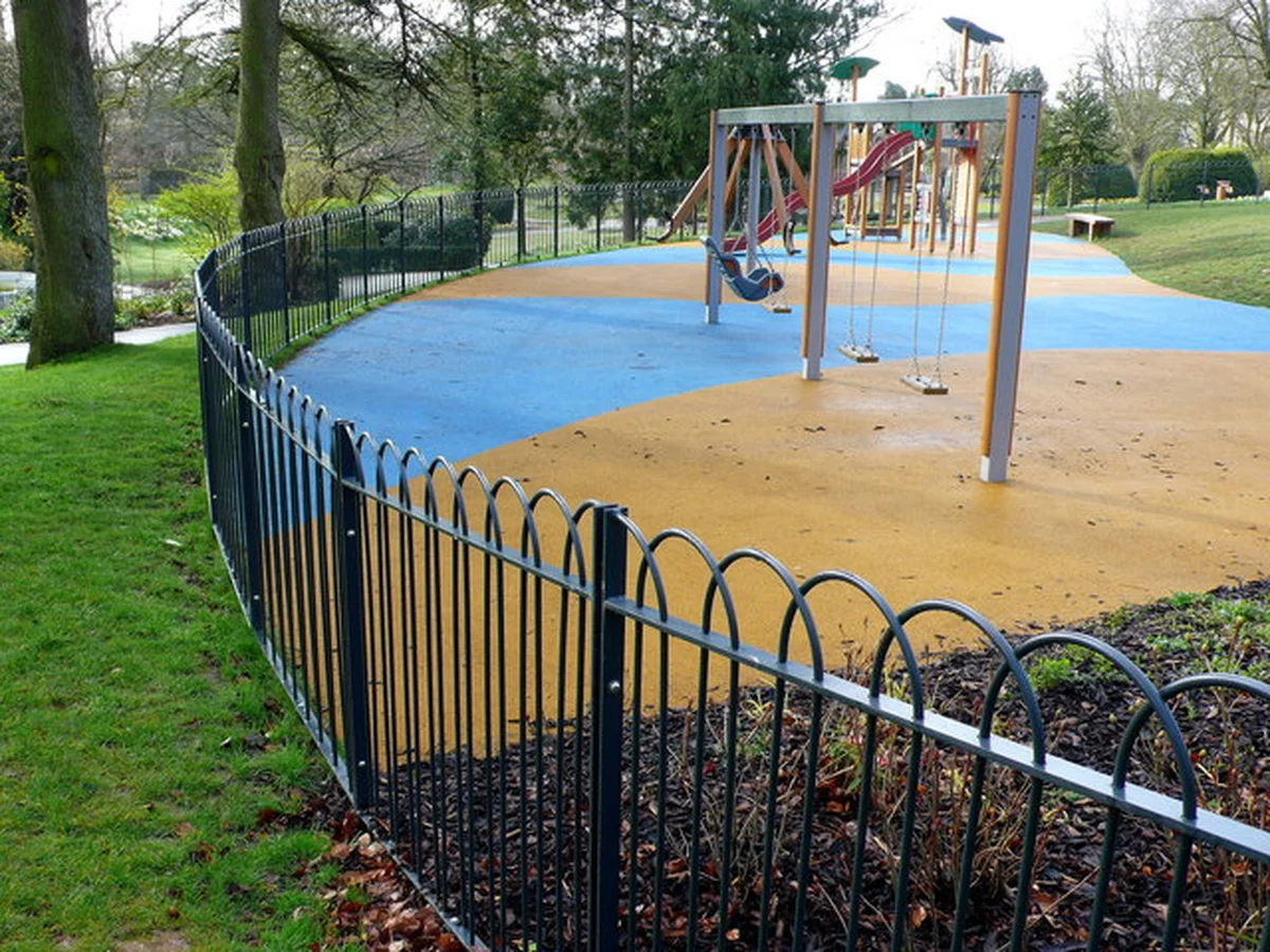 The fenced play area in Borough Gardens, Dorchester, with swings and a multi-play tower on a soft surface