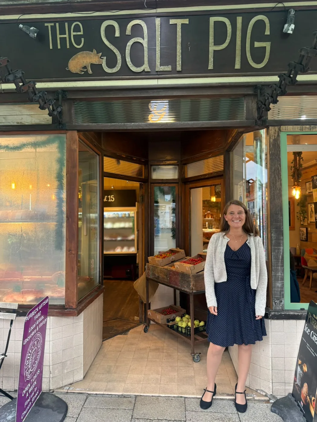 Vikki Slade MP standing in the doorway of The Salt Pig in Wareham, with crates of fruit on a trolley beside her