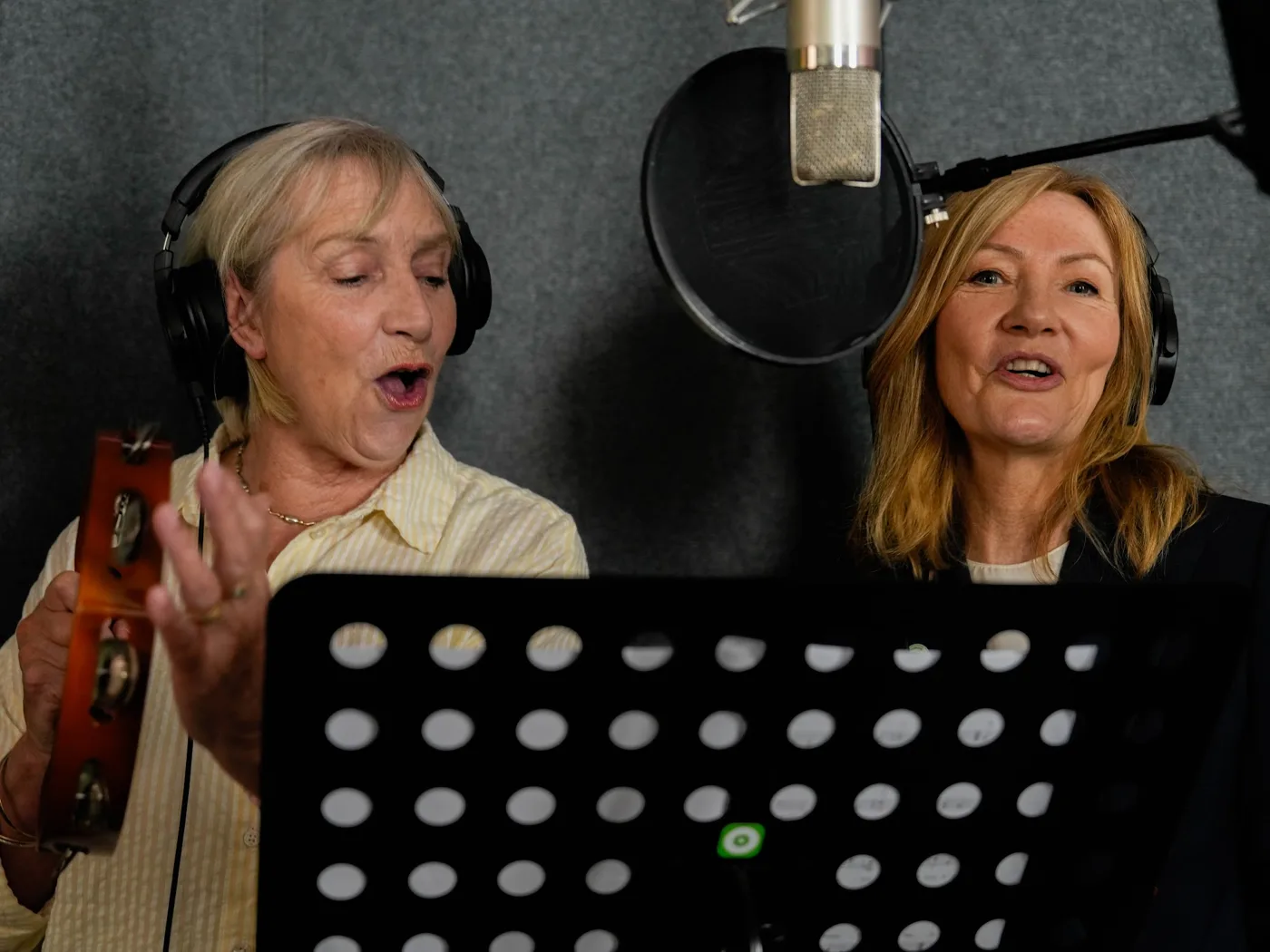 Pam Rhodes and Sally Chivers singing at a microphone in a recording booth