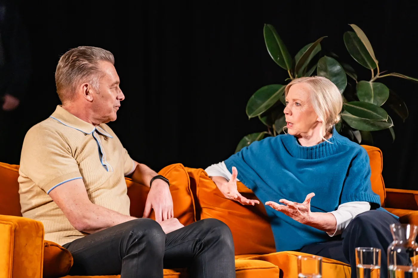 Two contributors to the People's Emergency Briefing in conversation on an orange sofa in a darkened studio