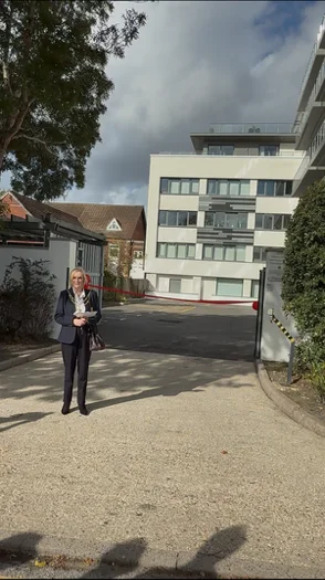 A woman holding a sheet of paper on the driveway in front of the Altitude block, with a red ribbon across the car park entrance behind her