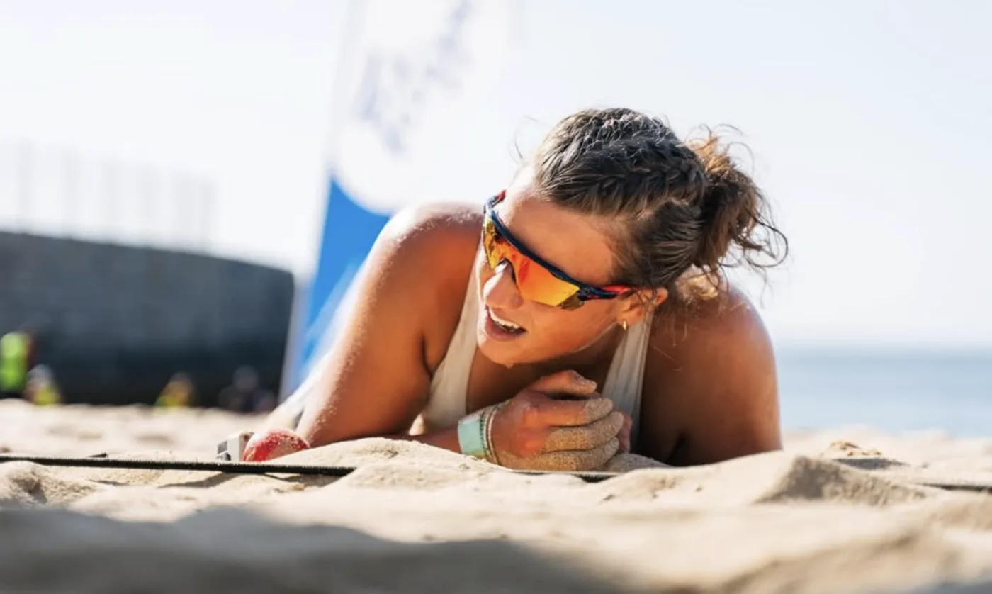Lexi Gill in sunglasses lying on the sand at a beach sprint event, smiling