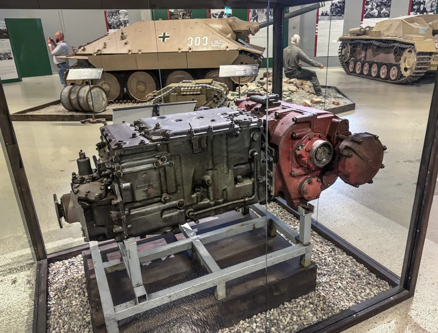A King Tiger gearbox, grey with a red housing at one end, on a metal stand in a display case at Arsenalen