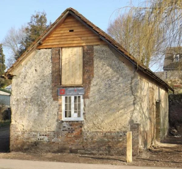 The cob and brick gable end of Tolpuddle Old Chapel, with a boarded upper window and a small paned window below, during its restoration